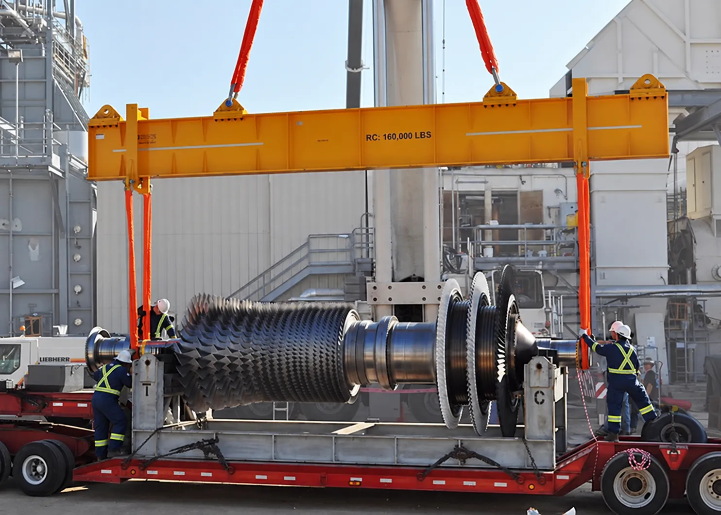 Workers handling an industrial gas turbine rotor during installation at an oil and gas facility.